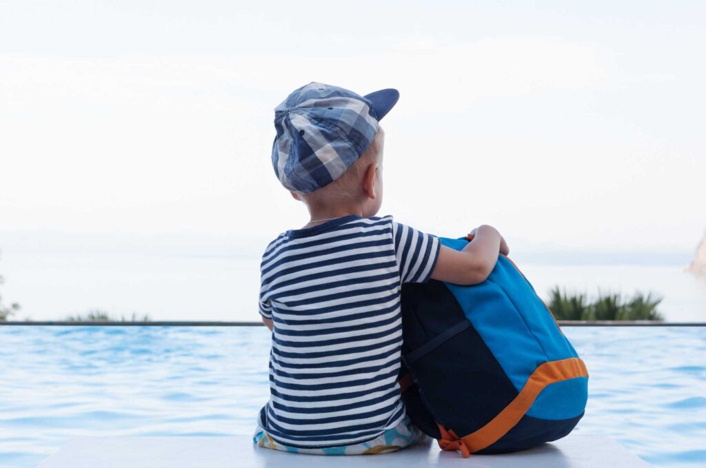 enfant garçon avec une casquette assis de dos et tenant un sac à dos